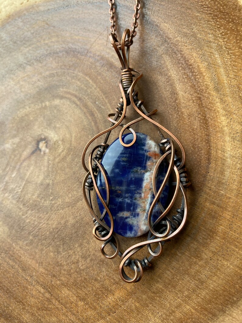 May include: A copper wire wrapped pendant featuring a blue and white gemstone. The pendant is attached to a copper chain.