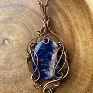 May include: A copper wire wrapped pendant featuring a blue and white sodalite gemstone. The pendant is attached to a copper chain.