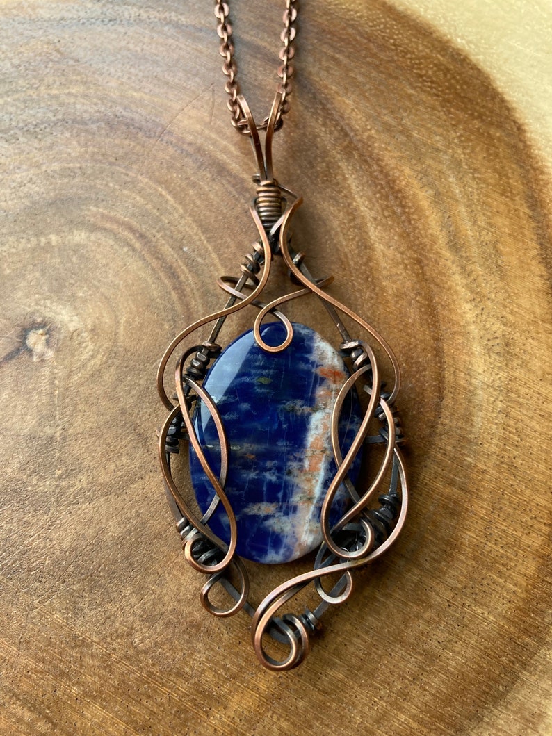 May include: A copper wire wrapped pendant featuring a blue and white sodalite gemstone. The pendant is attached to a copper chain.