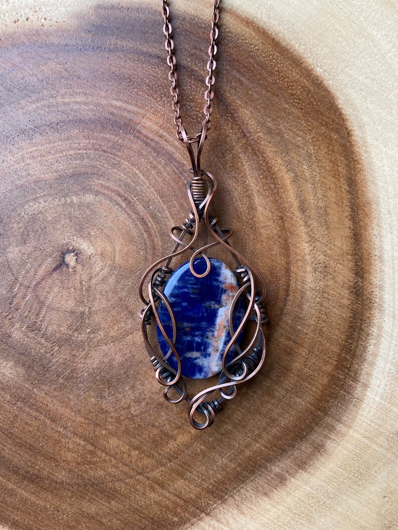 May include: A copper wire wrapped pendant featuring a blue and white gemstone. The pendant is attached to a copper chain.