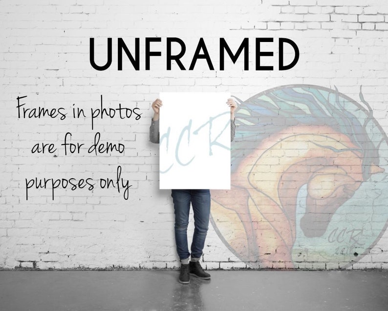 May include: A person holding a white poster with the word "UNFRAMED" printed in black letters. The poster is in front of a brick wall with a colorful painting of a horse's head. The text "Frames in photos are for demo purposes only" is written in black on the wall.