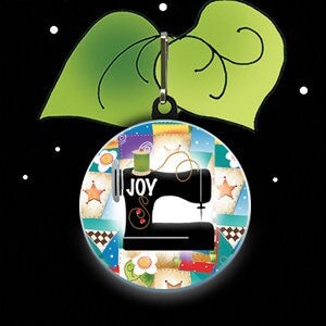 May include: A colorful zipper pull charm featuring a sewing machine with the word "JOY" on it. The charm is surrounded by a patchwork design with various colors and patterns.
