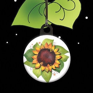 May include: A sunflower zipper pull charm with green leaves and a white background. The charm is attached to a silver zipper pull. The text "Jody's Zipper Pull Charms" is at the top of the image.