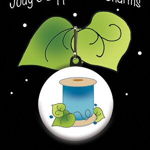 May include: A blue and white spool of thread with green leaves on a white background. The spool is attached to a silver zipper pull charm. The charm is surrounded by two green leaves with a swirl design.