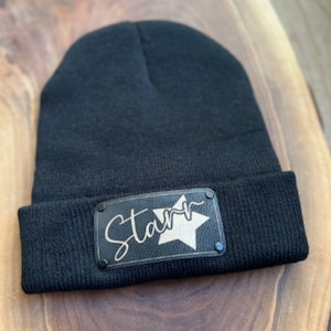 Könnte beinhalten: Schwarze Mütze mit einem schwarzen Leder-Patch, auf dem "Starr" in goldenen Buchstaben mit einem goldenen Stern steht.