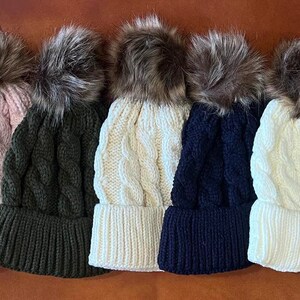 May include: Seven knitted winter hats with faux fur pom poms in various colors, including red, pink, green, white, and black.