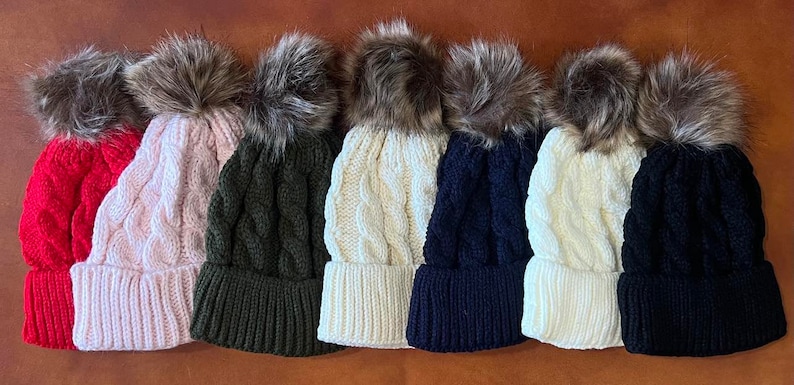 May include: Seven knitted winter hats with faux fur pom poms in various colors, including red, pink, green, white, and black.
