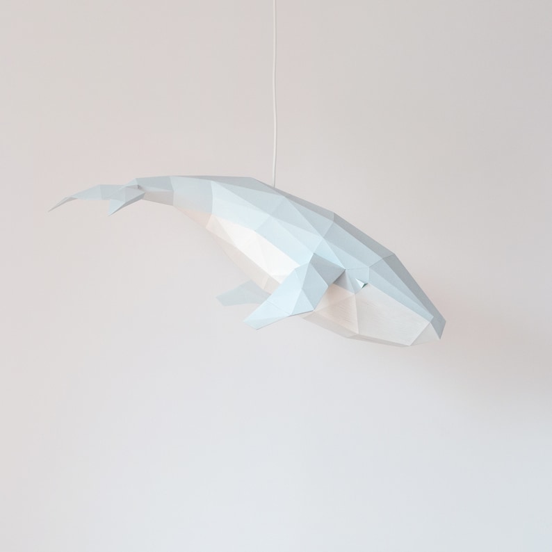 Puede incluir: Una escultura de ballena de papel blanco colgada del techo. La ballena est&aacute; hecha de papel doblado y tiene un dise&ntilde;o geom&eacute;trico.