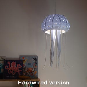 May include: A jellyfish-shaped pendant light. The light has a light blue, perforated dome with white dots and long, flowing, white paper-like streamers. The text "Hardwired version" is at the bottom of the image.