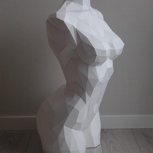 May include: A white, geometric, paper sculpture of a torso.
