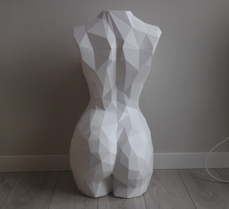 May include: White geometric sculpture of a human torso. The sculpture is made of paper and has a smooth, matte finish.