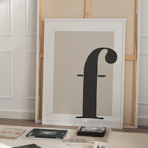 May include: A framed print with a beige background and a black stylized letter "f" in the centre. The print is in a white frame.