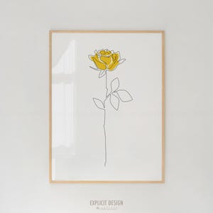 Puede incluir: Un dibujo minimalista de una rosa amarilla con un solo tallo y hojas. El dibujo está sobre un fondo blanco y enmarcado en un marco de madera claro.