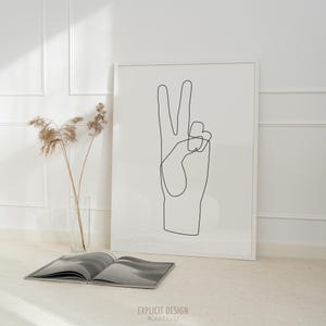 May include: A black and white line drawing of a hand making the peace sign. The drawing is framed and hanging on a white wall.