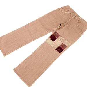 May include: A pair of light pink denim jeans with a patchwork design on the right knee. The patchwork is made of different coloured fabrics, including brown, white, and pink.