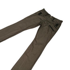 以下が含まれることがあります： 黒いジッパーのディテールとボタン留めが付いた濃い緑色のパンツです。