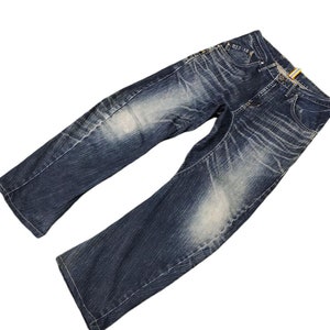 Può includere: Un paio di jeans blu denim con dettagli sbiaditi e consumati. I jeans hanno una vestibilità rilassata e una gamba dritta.