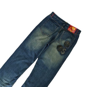 May include: Blue denim jeans with distressed details and patches on the back pockets.