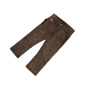 Puede incluir: Pantalón vaquero marrón con un detalle de cremallera en las costuras laterales y un pequeño parche de bandera de la Union Jack en el bolsillo delantero.