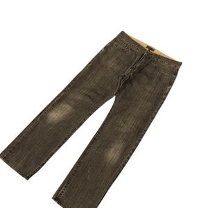 Könnte beinhalten: Eine verblasste schwarze Jeans. Die Jeans hat ein klassisches Fünf-Taschen-Design mit Knopf- und Reißverschluss. Der Denim hat ein abgenutztes Aussehen mit helleren Flecken auf den Oberschenkeln.