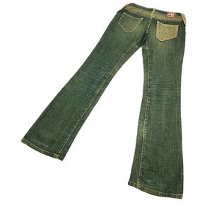 Könnte beinhalten: Eine dunkelgrüne Jeans mit einer dekorativen Gesäßtasche. Die Tasche hat ein goldenes Stickmuster.