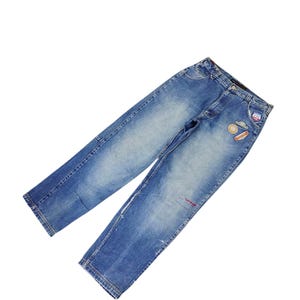 May include: Light blue denim jeans with patches and a distressed look. The jeans have a classic five-pocket design and a straight leg cut. Patches include a cloud, a hot dog, and a flag.
