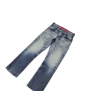 May include: Faded blue denim jeans with a classic five-pocket design. The jeans have a straight leg cut and show signs of wear with lighter patches. The waistband features a red interior lining.