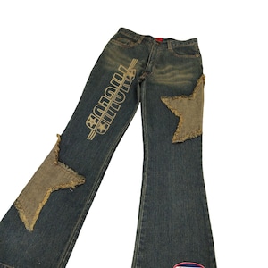 May include: Blue denim jeans with a star-shaped patch on the right leg and the word "PHCLUB" printed on the left leg. The jeans have a flared leg style.