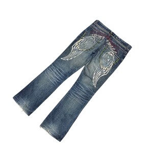 May include: Faded blue denim jeans with white angel wing designs on the back pockets. The jeans have a bootcut style and feature decorative stitching and colorful accents near the back waistband.