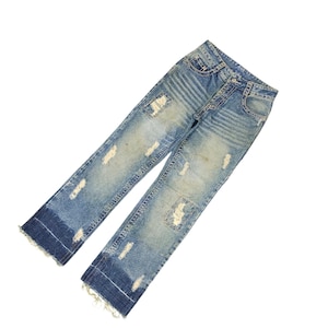 May include: Light blue denim jeans with distressed details, including ripped patches and faded areas. The jeans have a classic five-pocket design and a straight leg cut with frayed hems. The overall look is casual and worn.