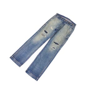 May include: Light blue denim jeans with distressed details, including ripped sections on the legs. The jeans have a classic five-pocket design and a button and zipper closure. The denim has a faded wash for a worn look.