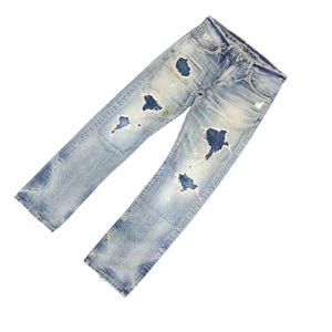 May include: Light blue denim jeans with distressed details, featuring multiple ripped sections. The jeans have a classic five-pocket design and a faded wash, giving them a worn-in appearance. The jeans are angled on a white background.