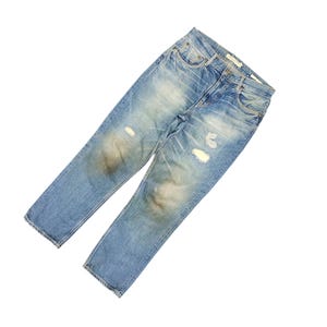 May include: Light blue denim jeans with distressed details, including faded patches and ripped areas. The jeans have a classic five-pocket design and a button and zipper closure. The denim has a worn appearance.