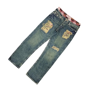 May include: Blue denim jeans with distressed details, featuring ripped patches on the knees. The jeans have a patterned waistband and a faded wash. The overall style is casual and worn.