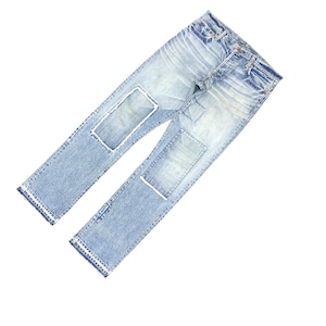 May include: Light blue denim jeans with distressed details and patches. The jeans have a classic five-pocket design, a button and zipper closure, and a straight leg fit. The patches are white and rectangular.