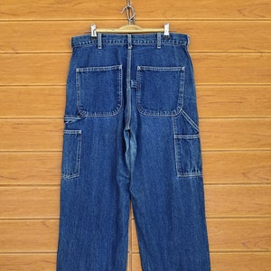 Puede incluir: Un par de pantalones de mezclilla azul de carpintero con múltiples bolsillos y un corte recto.