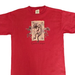 Könnte beinhalten: Rotes T-Shirt mit einem Aufdruck von amerikanischen Ureinwohnern, die vor einem braunen Teppich tanzen. Der Text "Grand Canyon" ist unter dem Aufdruck gedruckt.
