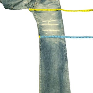 May include: Light blue denim jeans with distressed detailing. The jeans are measured with a yellow tape measure across the waist and a blue tape measure down the leg. The leg length is approximately 16 inches.