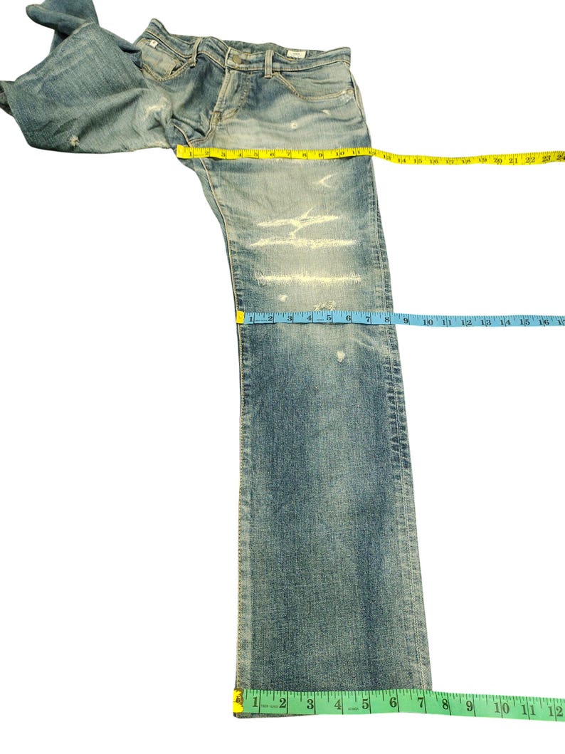 May include: Light blue denim jeans with distressed detailing. The jeans are measured with a yellow tape measure across the waist and a blue tape measure down the leg. The leg length is approximately 16 inches.