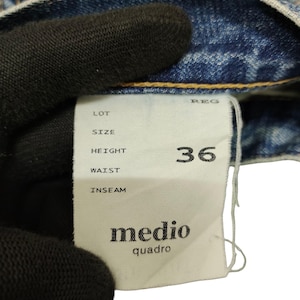Puede incluir: Primer plano de una prenda vaquera azul claro con una etiqueta blanca. La etiqueta muestra la talla 36 y la marca "medio quadro". El tejido vaquero muestra signos de desgaste.