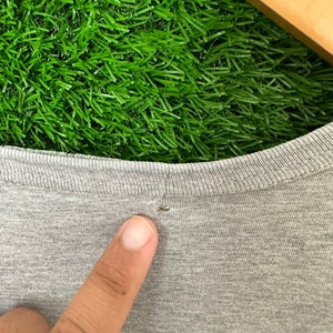 Może przedstawiać: Zbliżenie na szary t-shirt z małą dziurką w pobliżu dekoltu.