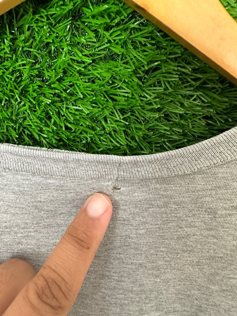 Może przedstawiać: Zbliżenie na szary t-shirt z małą dziurką w pobliżu dekoltu.