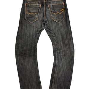 Op de afbeelding: Donkerblauwe denim jeans met een klassiek vijf-zakken ontwerp. Kenmerken zijn oranje stiksels, een leren patch en een subtiele uitlopende beenopening. De jeans hebben een versleten uiterlijk en een knoop- en ritssluiting.