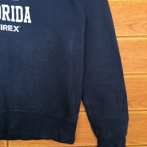 May include: A dark blue sweatshirt with white text that reads "1975" and "Florida" with the word "IREX" underneath.