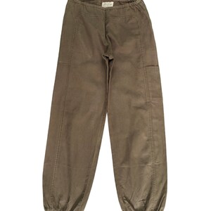 May include: A pair of brown cargo pants with a drawstring waist and elastic cuffs. The pants have two large pockets on the sides.