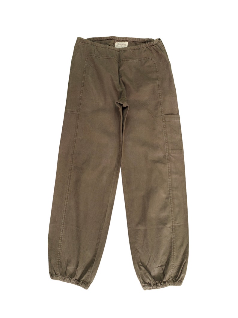 May include: A pair of brown cargo pants with a drawstring waist and elastic cuffs. The pants have two large pockets on the sides.