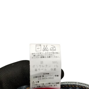 May include: A close-up of a clothing tag with Japanese text and care symbols. The tag indicates the material composition: 99% cotton and 1% polyurethane. It also includes washing instructions and a warning about color transfer.
