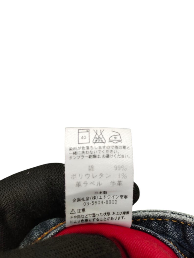 May include: A close-up of a clothing tag with Japanese text and care symbols. The tag indicates the material composition: 99% cotton and 1% polyurethane. It also includes washing instructions and a warning about color transfer.