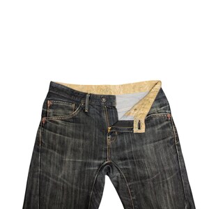 Op de afbeelding: Donkerblauwe denim jeans met een gedeeltelijk open rits. De jeans hebben een klassiek ontwerp met vijf zakken, met zichtbare stiksels in een contrasterende kleur. De binnenkant van de tailleband heeft een patroonstof.
