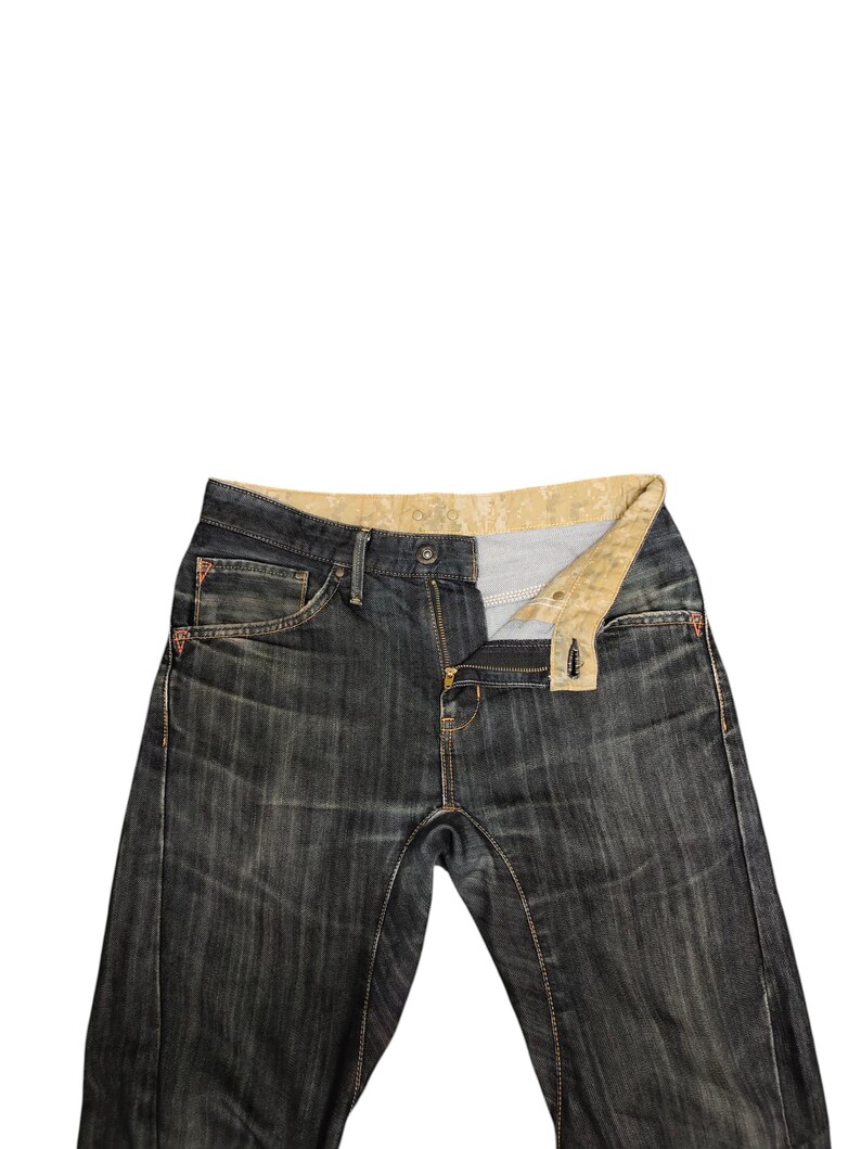 Op de afbeelding: Donkerblauwe denim jeans met een gedeeltelijk open rits. De jeans hebben een klassiek ontwerp met vijf zakken, met zichtbare stiksels in een contrasterende kleur. De binnenkant van de tailleband heeft een patroonstof.